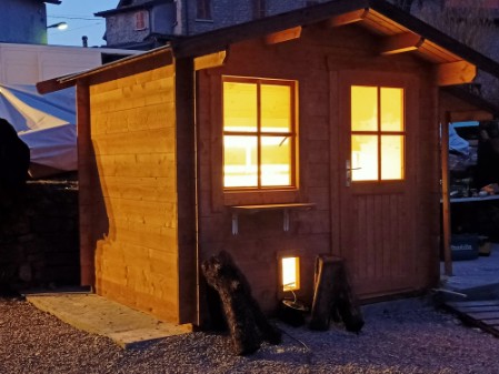 foto notturna di casetta per gatti interno illuminato visubiloe da porta e finestra con vetri, una gattaiola in basso a lato porta